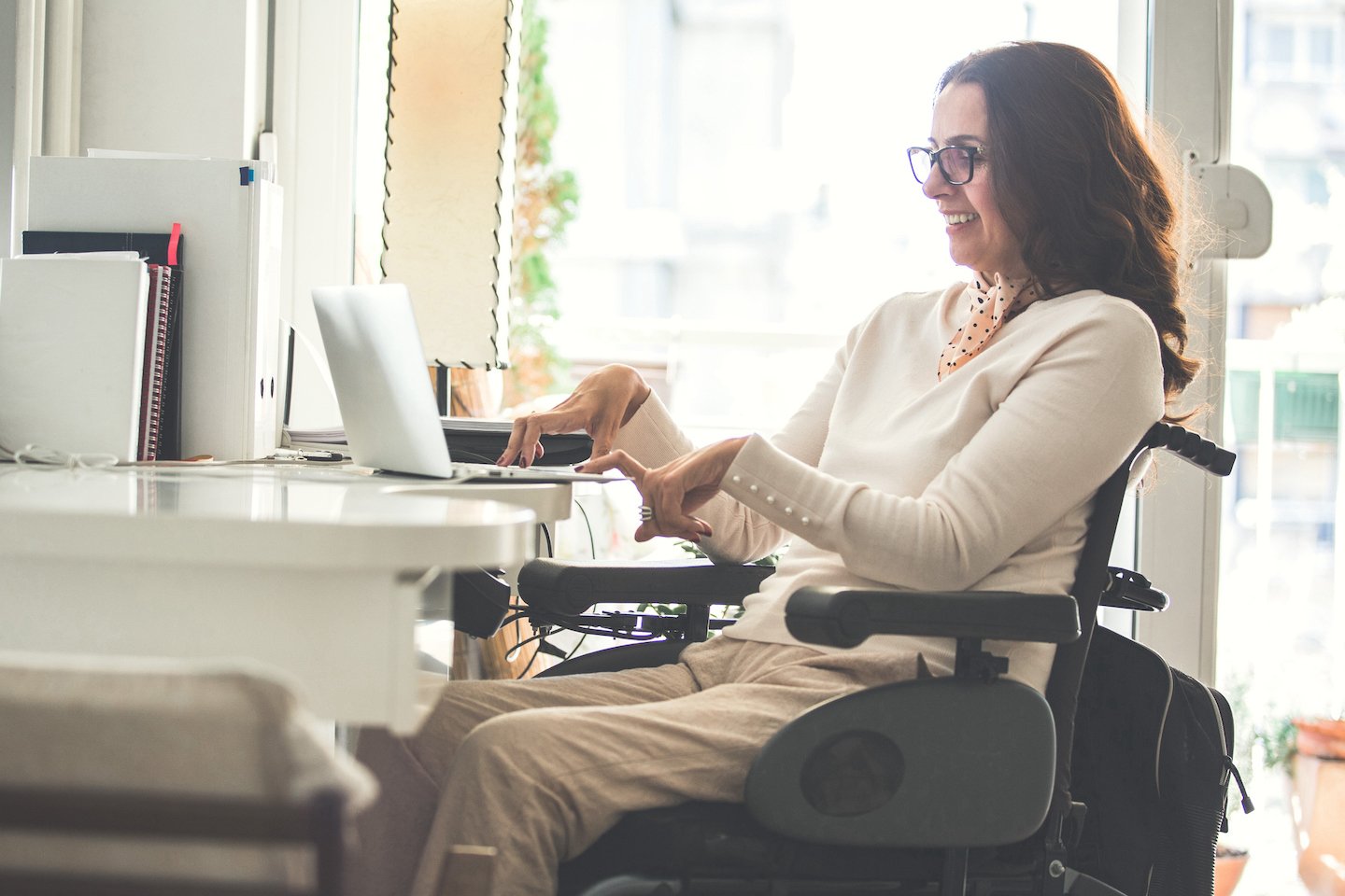 a disabled young woman in wheelchair working in office with laptop