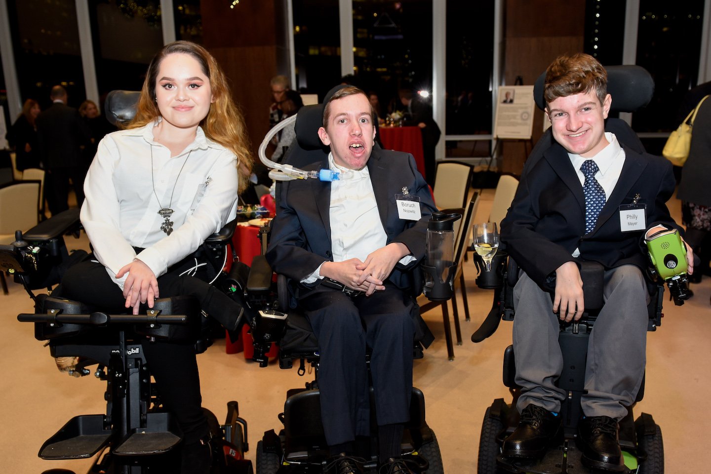 two disabled boy and one disabled girl sitting on wheelchairs and looking at the camera