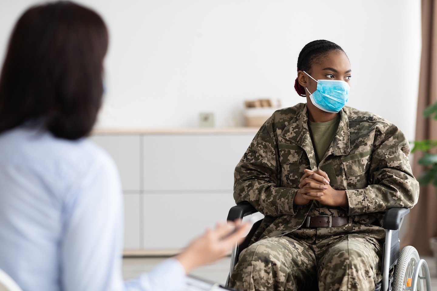 Depressed black military woman in wheelchair having therapy session with psychologist