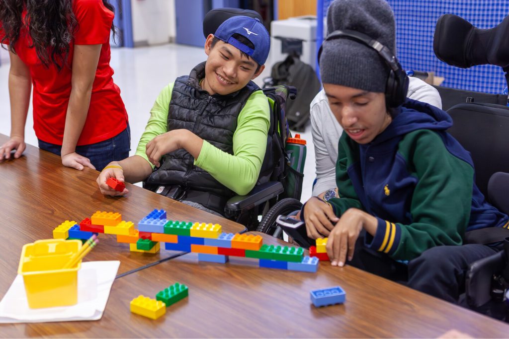 Two young men with disabilities in wheelchairs building Lego bridges.