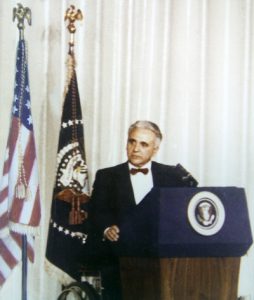 An image of the founder of The Viscardi Center and the Henry Viscardi School, Dr. Henry Viscardi, Jr. a man with white hair and a disability sitting in front of a podium wearing a suit and bowtie. 